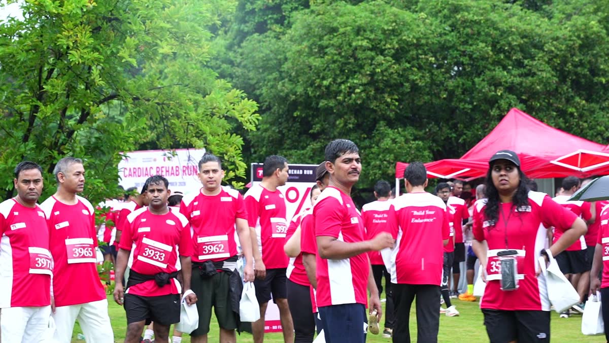 Runners in red Cardiac Rehab Run shirts at the drinks area in Sanjeevaiah Park, with the 6% board behind them