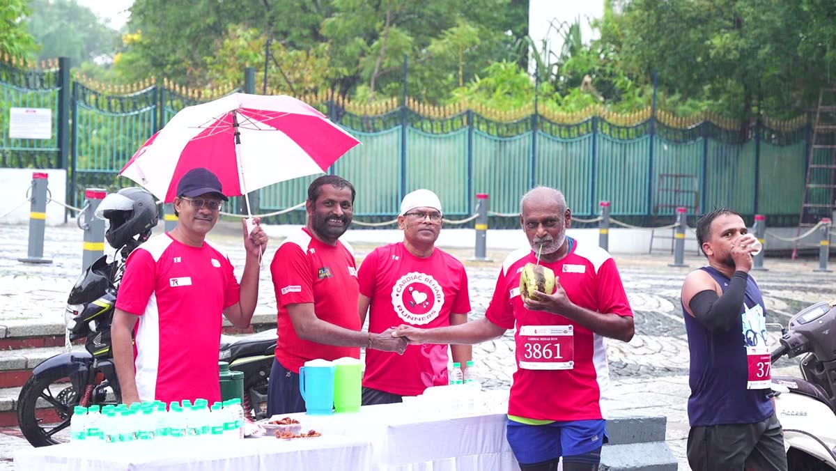 An older runner drinks from a tender coconut and shakes hands with a volunteer at a Cardiac Rehab Run aid table