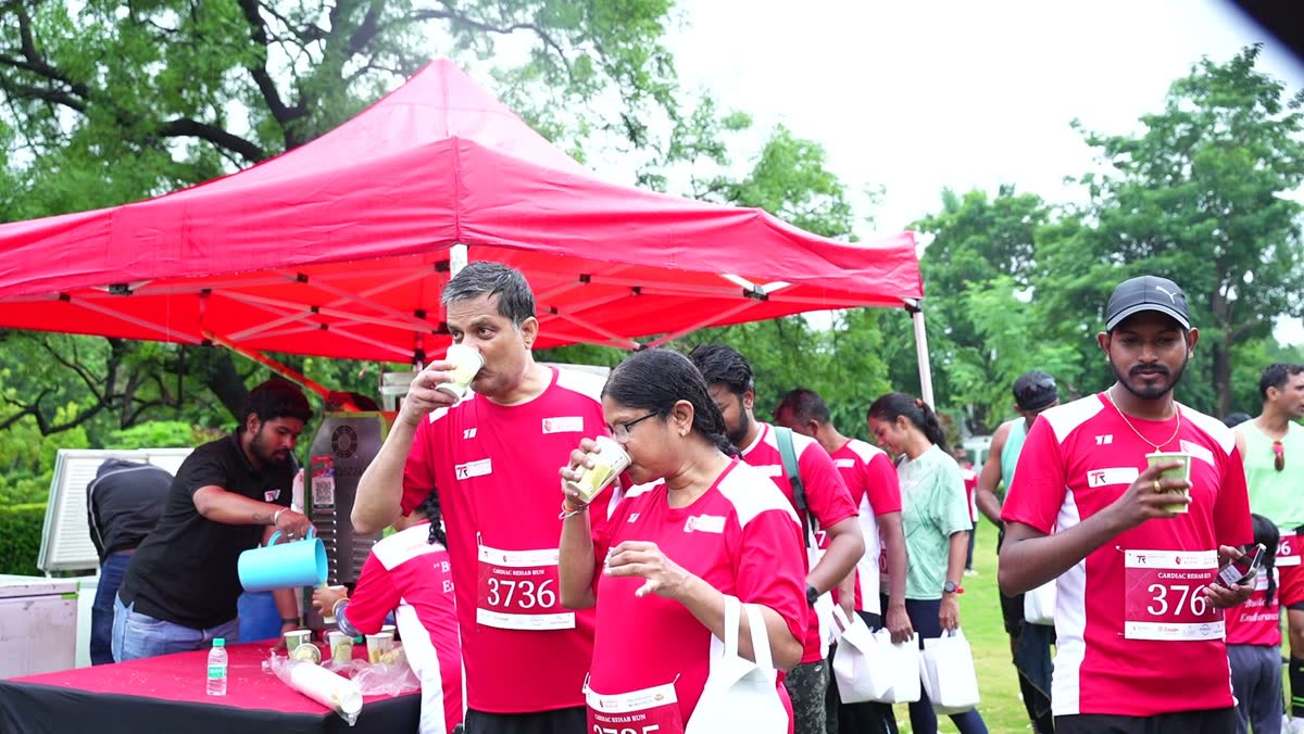 Runners drink fresh sugarcane juice under a red canopy while a volunteer pours more from the juice machine