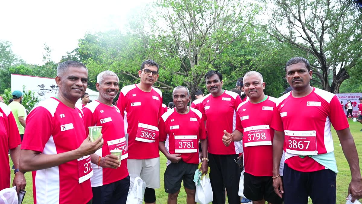 Seven runners in red Cardiac Rehab Run shirts and bibs, two holding cups of sugarcane juice